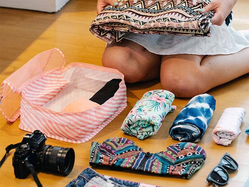 persona sentada en el suelo empacando ropa y accesorios en un cubo de embalaje