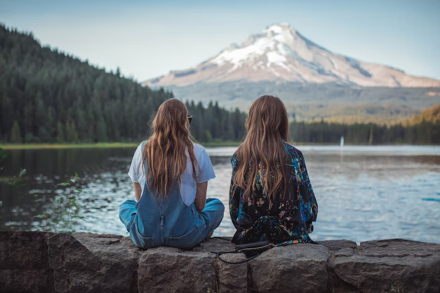 dos mujeres sentadas en una roca frente a un lago y una montaña
