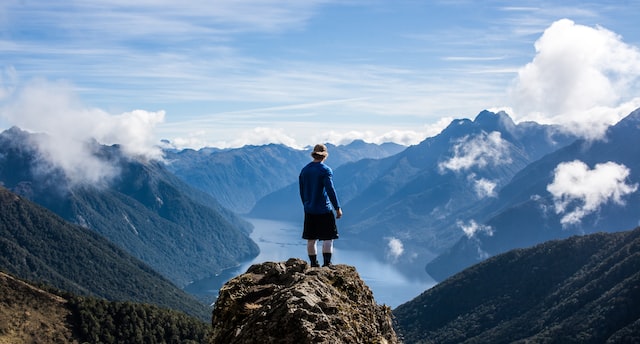 hombre de pie encima de una piedra de gran altura en el Parque Nacional de Fiordland en viaje a Nueva Zelanda