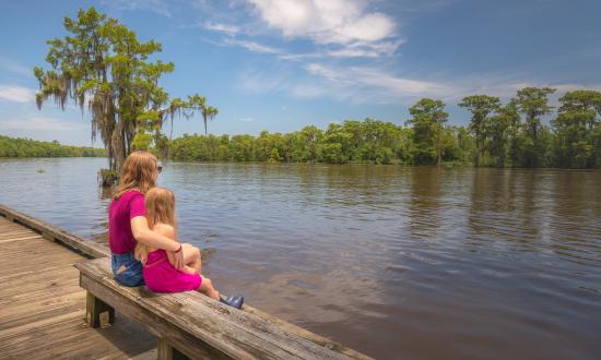 Una dama y una niña de rosa sentadas junto al río.