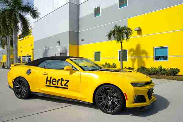 Camero amarillo con la marca Hertz fuera del edificio Hertz